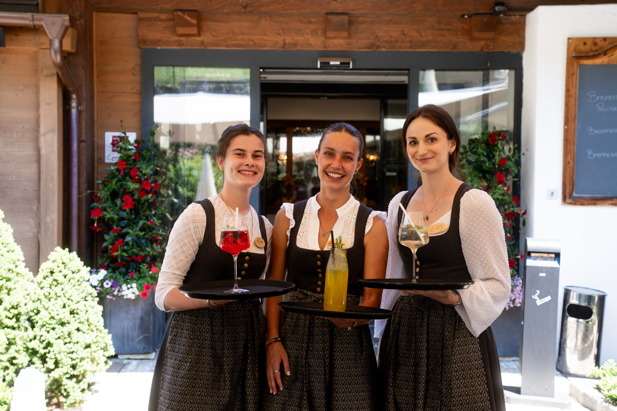 Three waitresses in dirndls serving drinks in front of a traditional restaurant