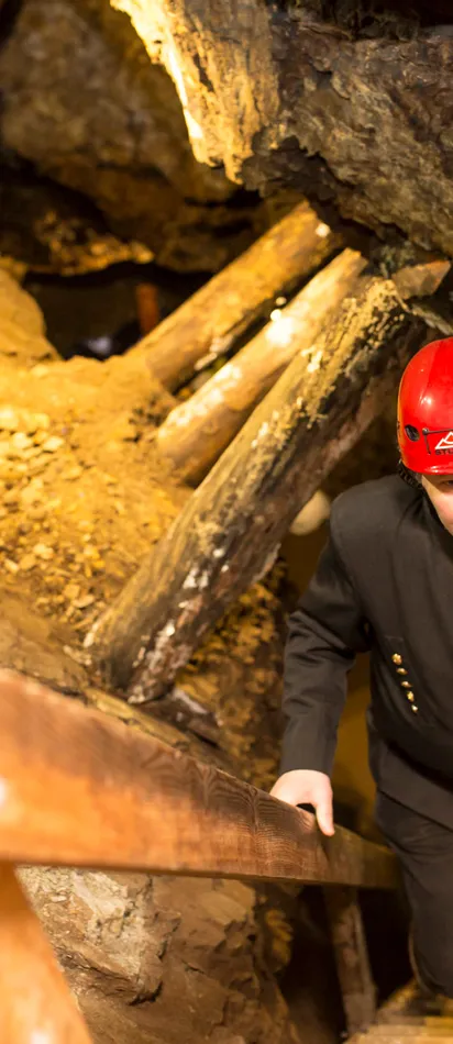 Bergmann mit rotem Helm steigt Holztreppe in historischem unterirdischem Bergwerk hinauf