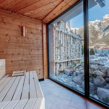 Wooden sauna interior with panoramic window view of snowy alpine mountains