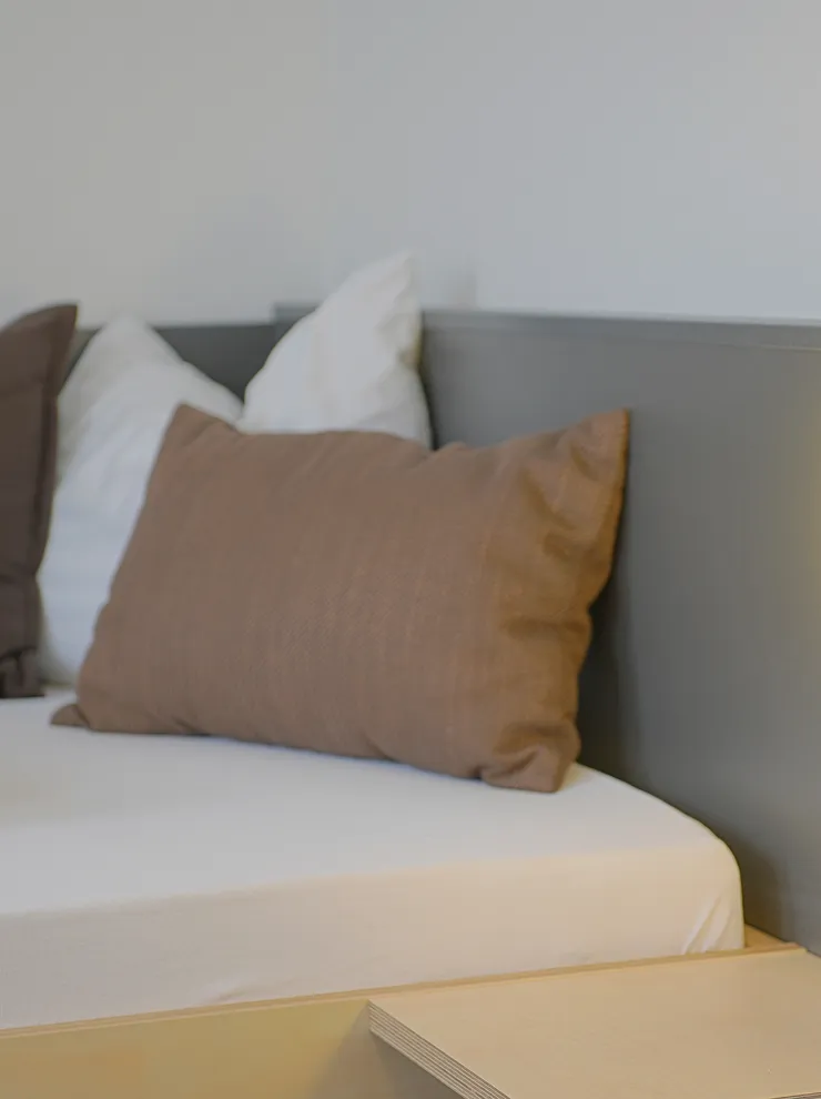 Modern bed with white and brown pillows next to illuminated wall lamp