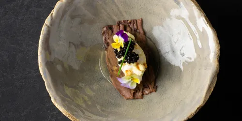 Gourmetfleischgericht mit Kaviar und essbaren Blüten auf handgemachtem Keramikteller