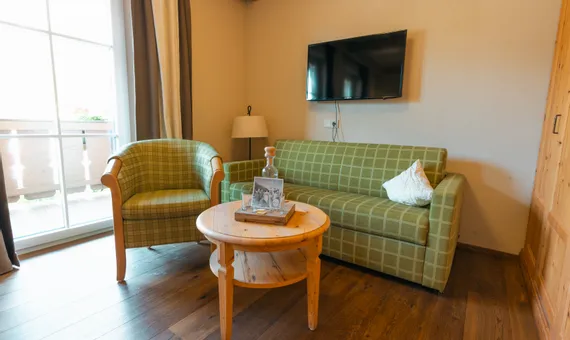 Cozy hotel room with green checkered sofa, armchair, round wooden table and wall-mounted TV