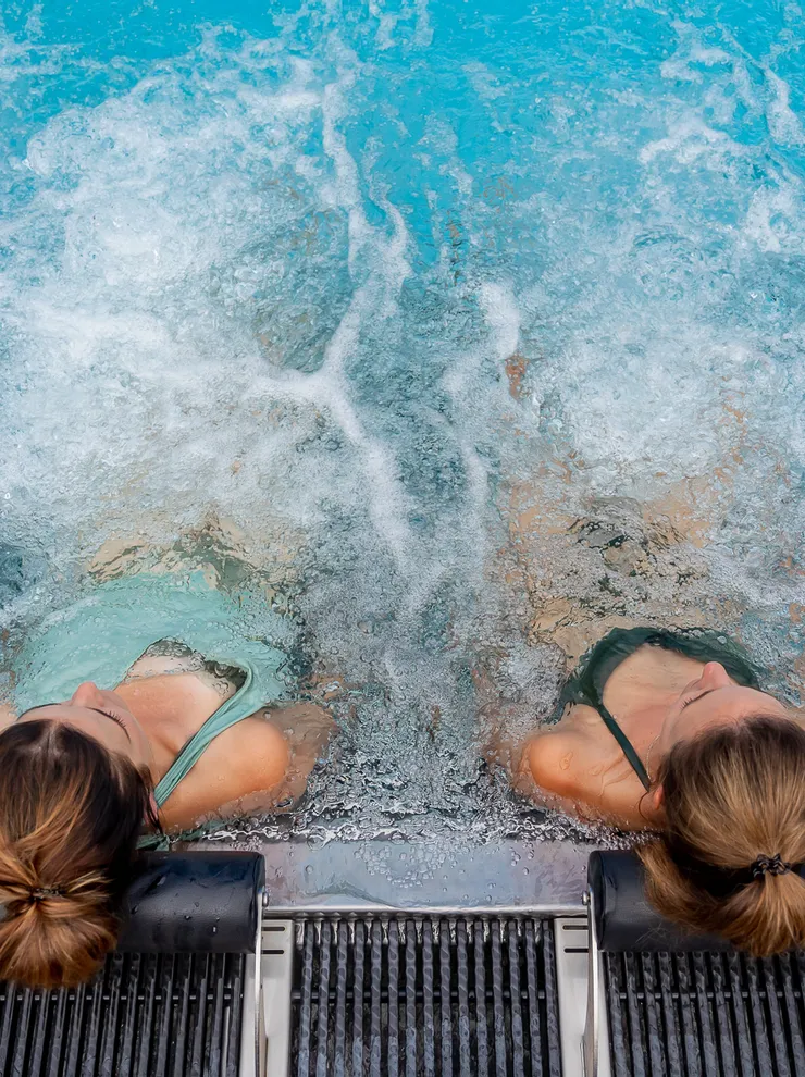 Zwei Frauen entspannen auf Poolliegen im sprudelnden Whirlpool eines Spas