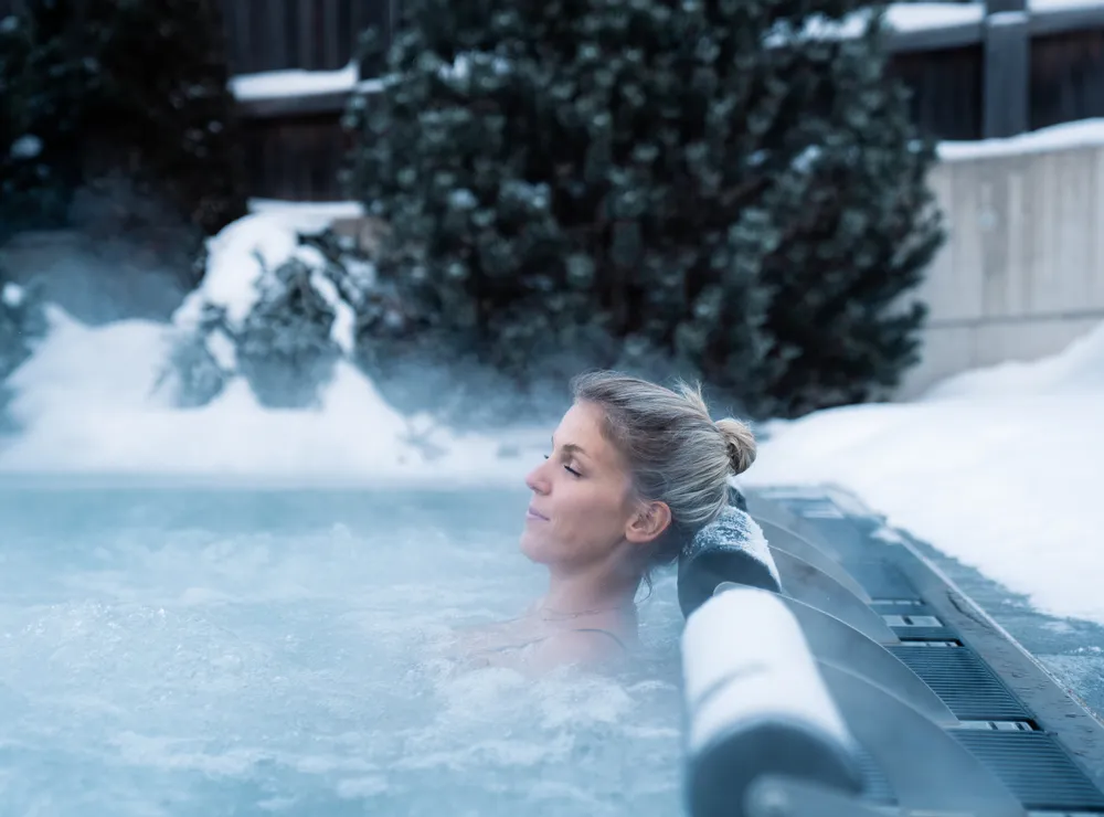 Frau entspannt in einem Außenwhirlpool umgeben von Schnee im Winter