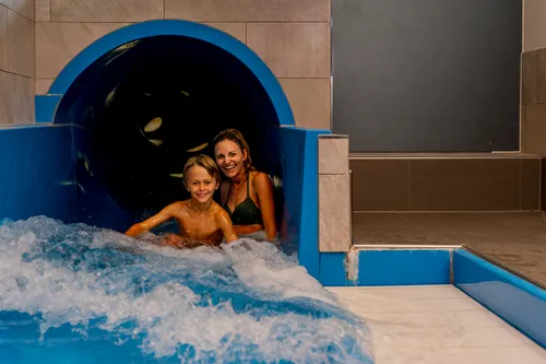 Lächelnde Mutter und Sohn kommen aus der Indoor-Wasserrutsche ins Becken