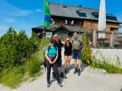 Group of hikers posing in front of a mountain hut on a sunny day