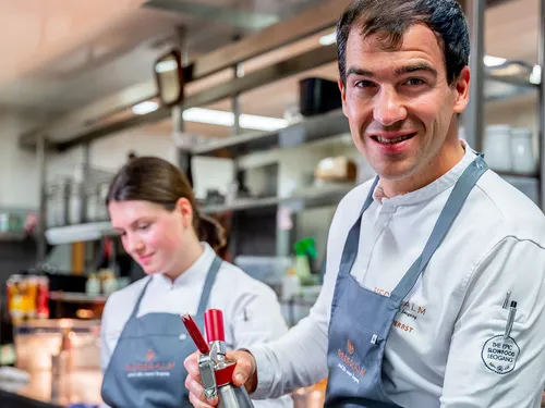 Smiling chef using a cream whipper in a professional kitchen with ceramic bowls in front