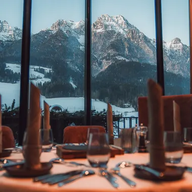 Elegant gedeckter Restauranttisch mit Blick auf schneebedeckte Alpen durch großes Fenster