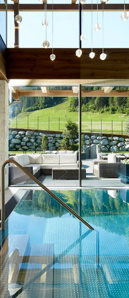 Luxuriöser Innenpool mit Sonnenliegen und Blick auf grüne Alpenlandschaft