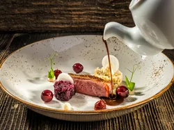 Gourmet duck breast with red cabbage, cherries, purée, and sauce on rustic ceramic plate