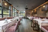 Modern restaurant interior with large windows, pink velvet chairs, and neatly set tables
