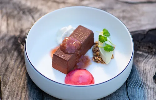 Schokoladendessert mit Eis, Obstkompott und Sahne auf weißem Teller auf Holztisch