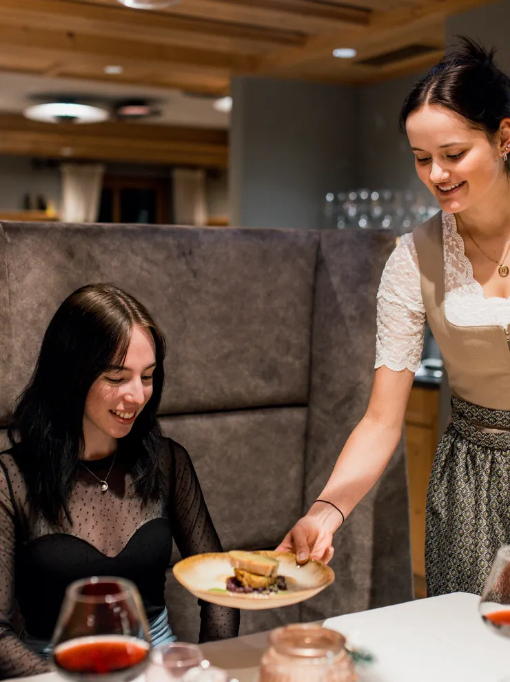 Waitress in traditional dress serving a dish at a cozy restaurant table