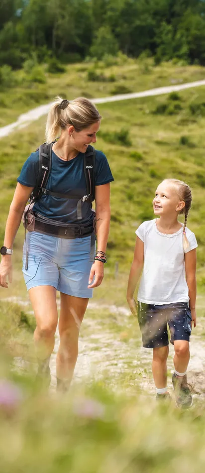 Familie wandert auf Bergpfad durch grüne Wiese an einem sonnigen Tag