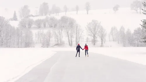 Zwei Personen halten Händchen beim Schlittschuhlaufen auf einem gefrorenen Weg im verschneiten Winterwald