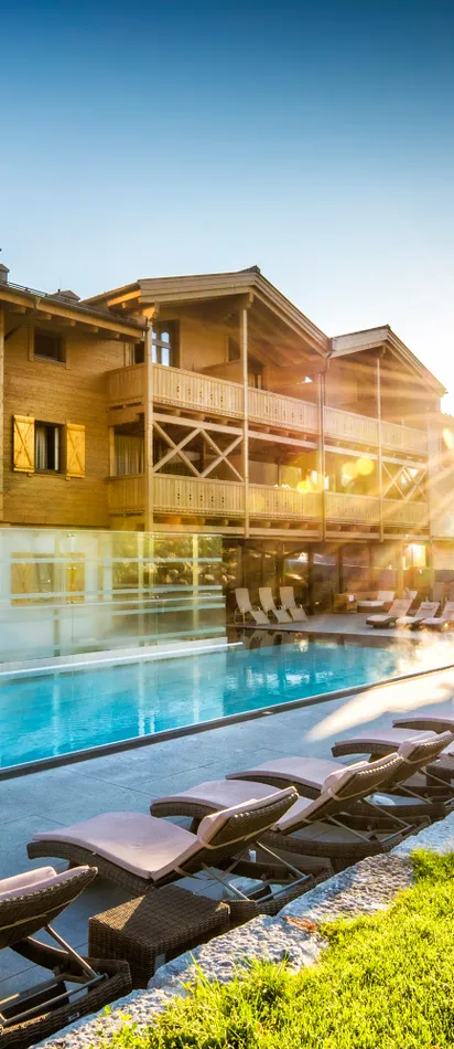 Luxuriöses Alpenresort mit Außenpool, Sonnenliegen und Bergblick bei Sonnenaufgang