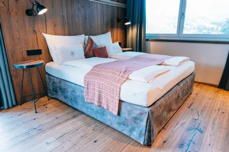 Modernes Hotelzimmer mit Doppelbett, Holzwand und großer Fensterblick auf Berge