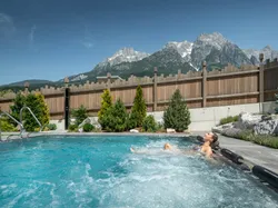 Woman relaxing in outdoor whirlpool with mountain view and wooden privacy fence