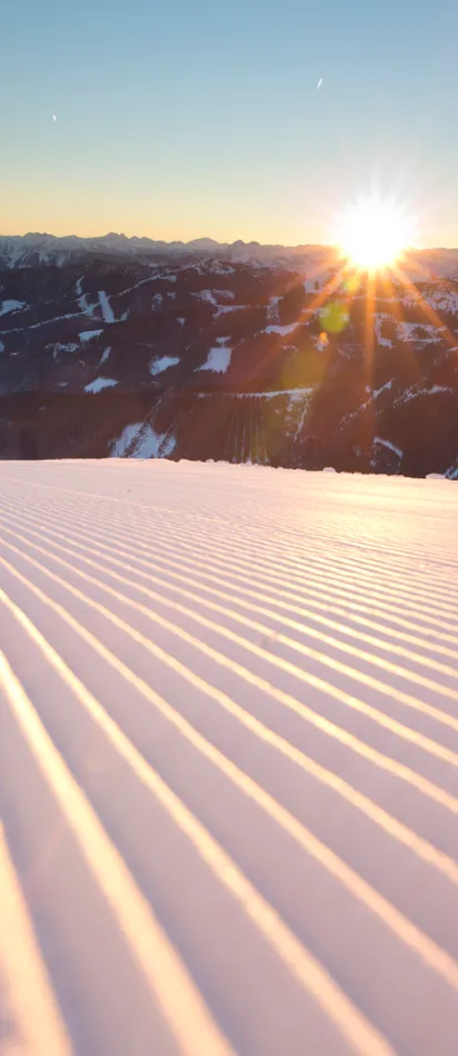 Freshly groomed ski slope at sunrise in snowy mountain landscape
