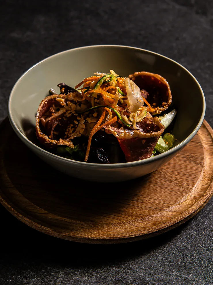 Asiatische Nudelschale mit frittierten Röllchen, Gemüse und Sesam auf dunklem Untergrund