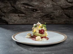 Gourmet-Dessert mit Biskuit, Creme, Kirschen und essbaren Blüten auf Keramikteller