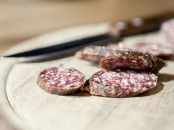 Aufgeschnittene luftgetrocknete Salami auf einem Holzbrett mit Messer im Hintergrund