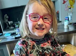 Lächelndes Kind mit Brille hält Karton mit bunt gefärbten Ostereiern in Küche