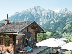 Berghütte mit Außenterrasse und Blick auf alpines Tal und zerklüftete Gipfel