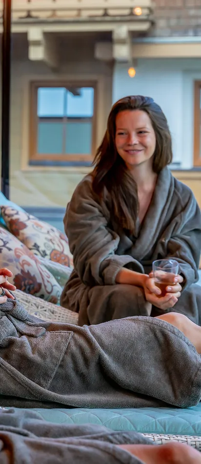 Drei Frauen entspannen in Spa-Liegen mit Bademänteln und Tee in der Hand