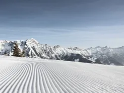 Frisch präparierte Skipiste vor verschneiten Alpen unter klarem Himmel
