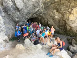 Wandergruppe vor einem felsigen Höhleneingang bei sonnigem Outdoor-Abenteuer