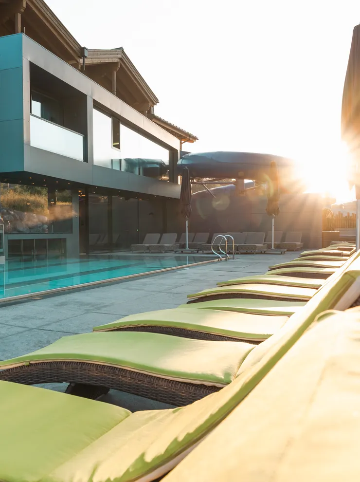 Moderner Hotelpool mit grünen Liegestühlen und Sonnenschirmen bei Sonnenaufgang