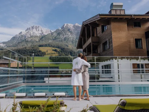 Couple in bathrobes at alpine resort pool with scenic mountain view