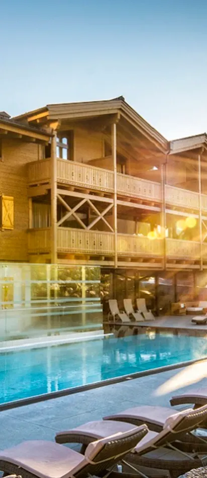 Luxuriöses Alpenresort mit Außenpool und Sonnenliegen bei Sonnenaufgang