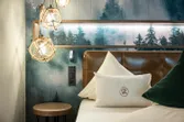 Modern hotel room with forest-themed wallpaper, leather headboard and decorative lighting