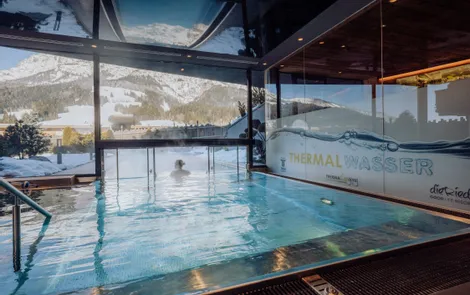 Innen-Thermalbecken mit Bergblick und badender Person im Winterresort