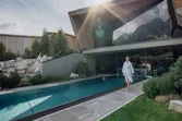 Frau im Bademantel geht am Außenpool eines modernen Wellnesshotels entlang