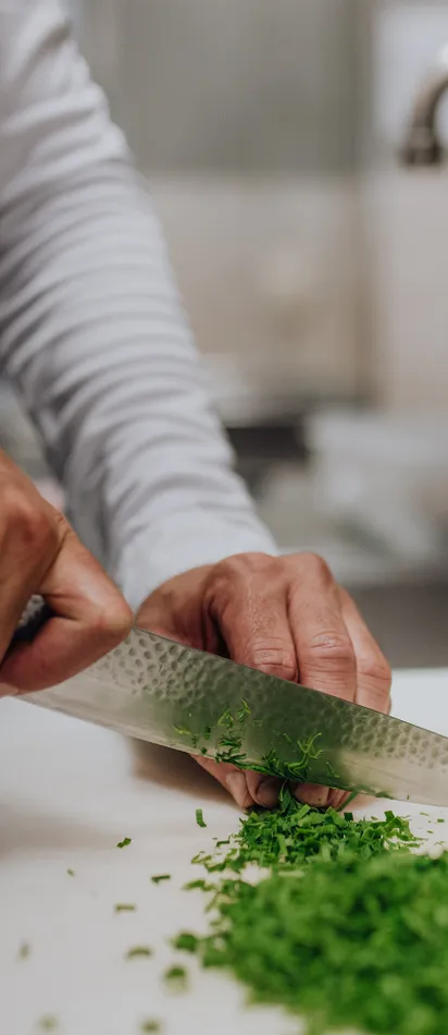 Chef chopping fresh chives with a large kitchen knife on a white cutting board
