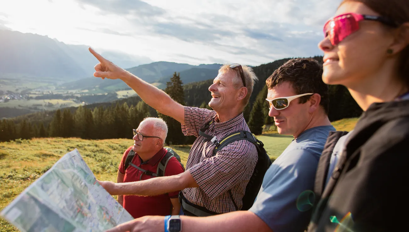 Group of hikers reading a map and pointing toward mountains in scenic alpine landscape