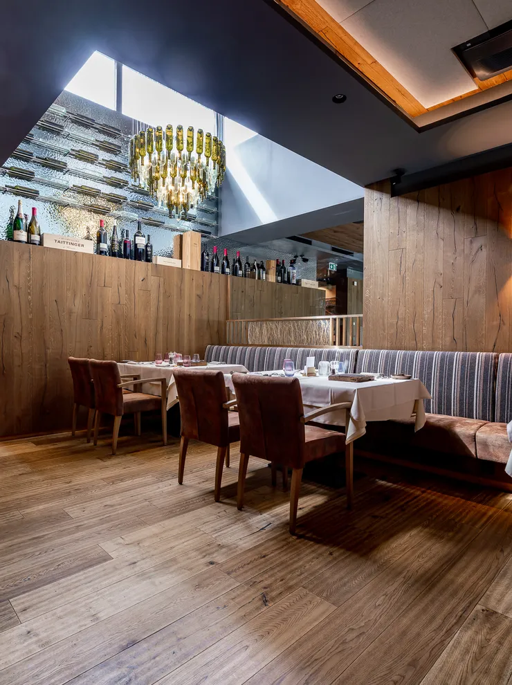 Elegant restaurant interior with wooden walls, wine bottles, and a chandelier made of glass bottles
