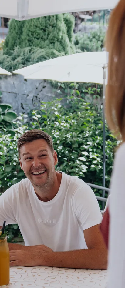 Smiling couple sitting at outdoor café table with drinks, talking to server