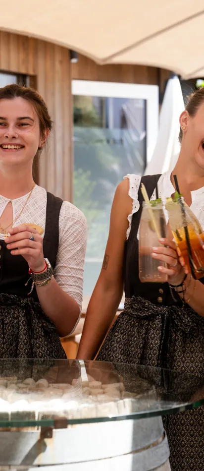 Smiling women in traditional dirndl dresses holding summer cocktails outdoors