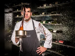 Chef in striped apron holding pot with caramel splash in modern wine cellar