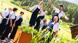 Happy kitchen team in uniforms enjoying sunshine in herb garden with alpine backdrop