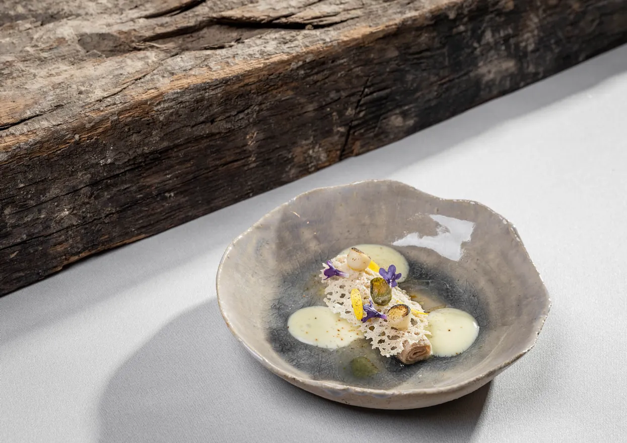 Gourmetgericht mit cremiger Soße, essbaren Blüten und Kräutern in grauer Keramikschale