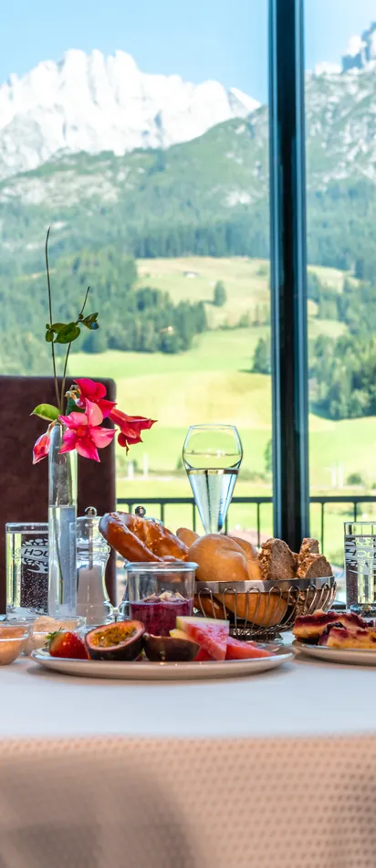 Breakfast table with pastries and fruit in front of panoramic alpine mountain view