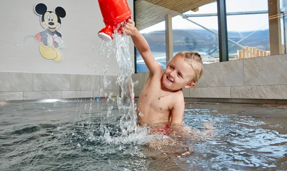 Smiling child playing with red watering can in indoor kids pool