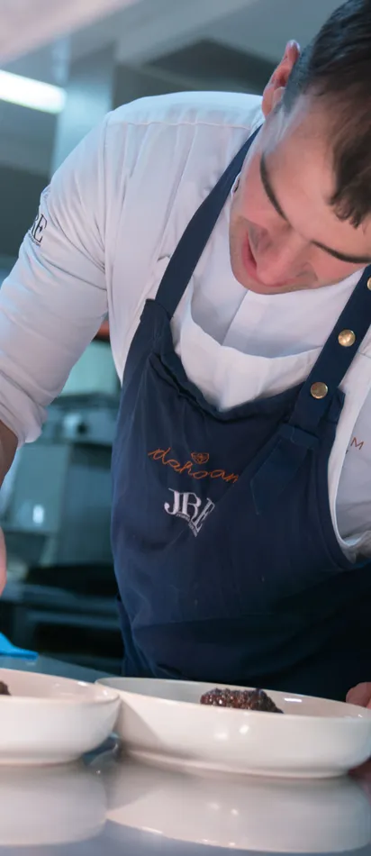 Chef plating gourmet dish in a busy professional kitchen