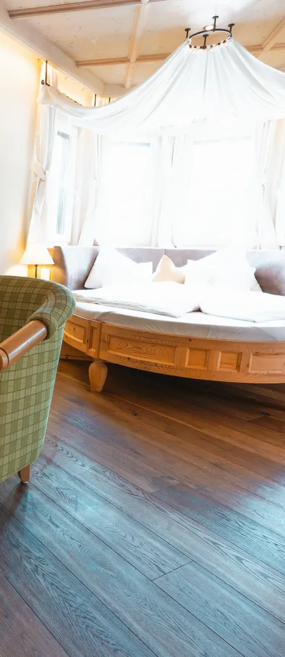 Cozy hotel room with green armchairs, round wooden table, and canopy bed by bright windows
