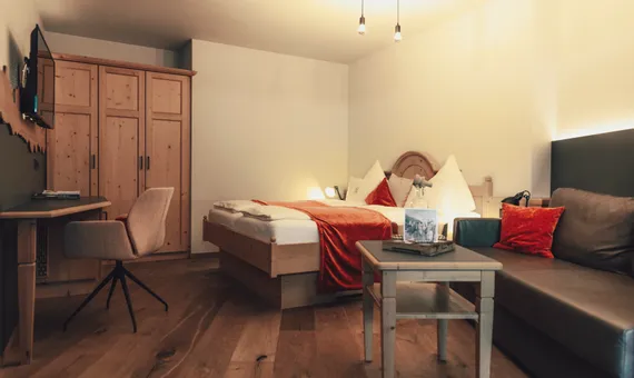 Cozy hotel room with wooden floor, double bed, sofa and writing desk